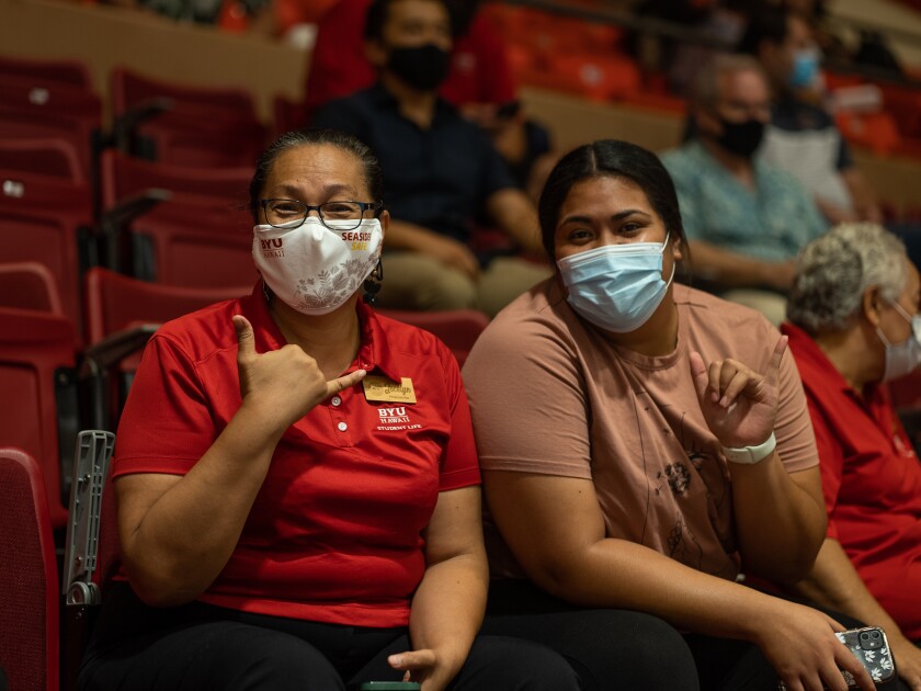 landscape shot of two women wearing masks seated in the CAC and holding up a shaka sign