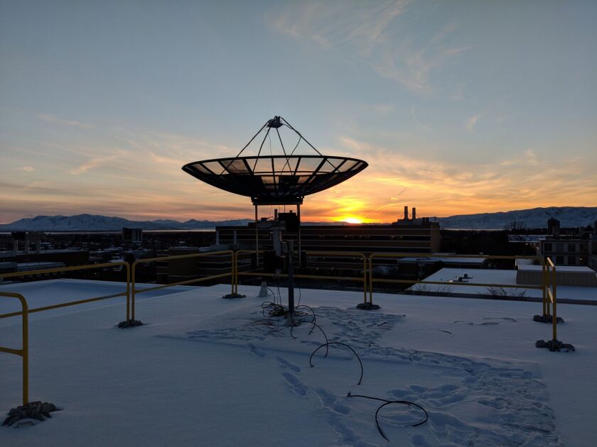 An image of a satellite on a roof with the sun setting in the background