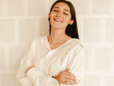 Ivy Griffiths smiles in front of a white brick wall. Her arms are folded and she is wearing a white button-up blouse.