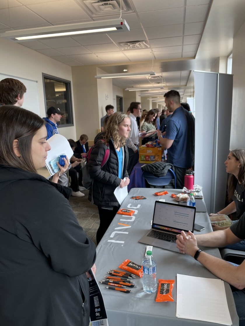 A pale student talks to a recruiter at a booth while another student looks on.