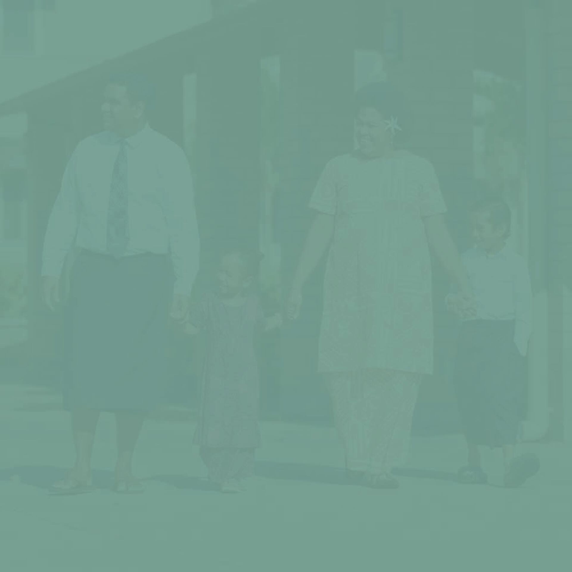 A family of four, including two adults and two children, walks together outdoors in front of a building, holding hands.