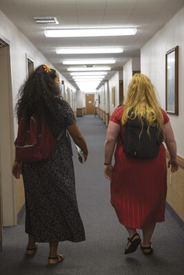 portrait shot of the backs of two sister missionaries wearing backpacks and walking down the hallway of the BYUH Stake Center