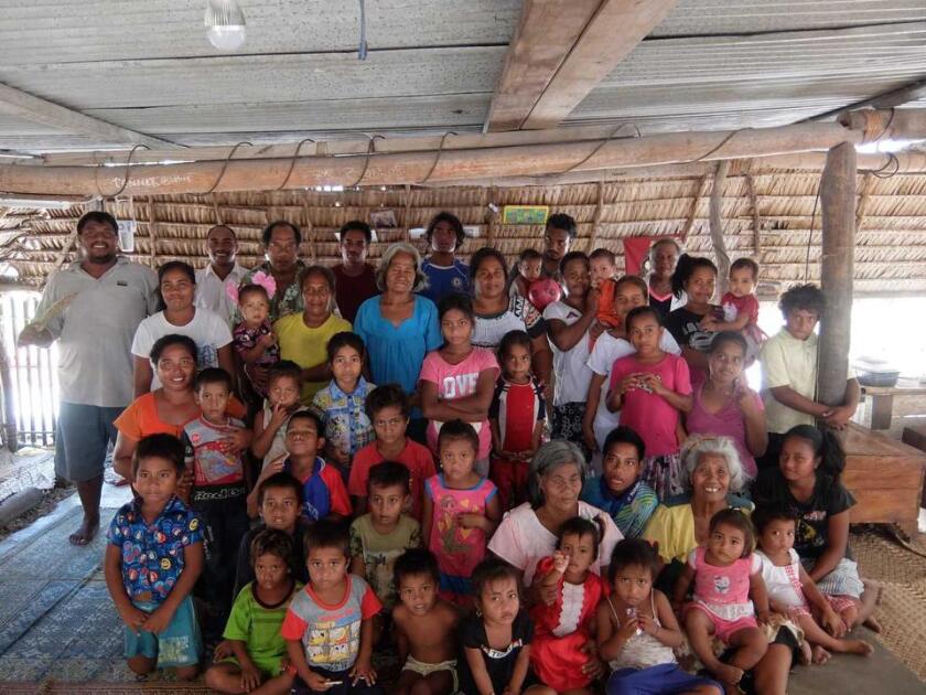 Kiribati people of all ages gather in a home with mats smiling together.