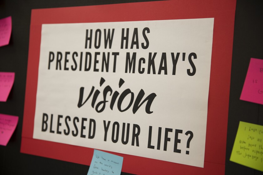 A piece of white paper with bolded black words: "How has President McKay's vision blessed your life?" with a red frame and pink, green, and blue sticky notes surrounding it with students answers to that question written on them.
