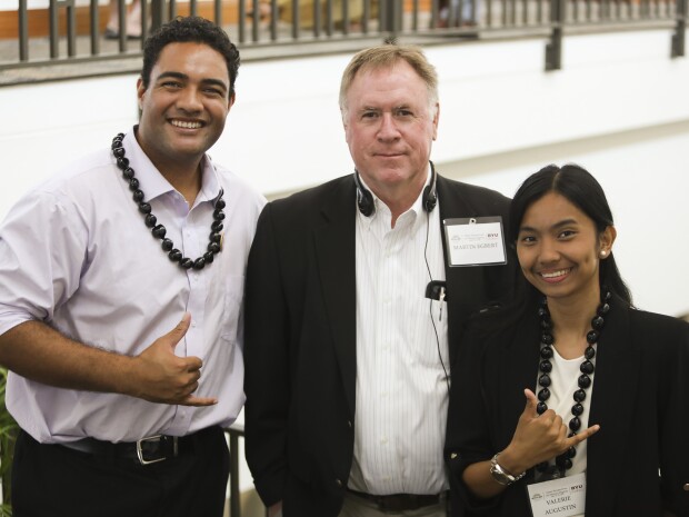 three people smiling at the camera holding up hand sign
