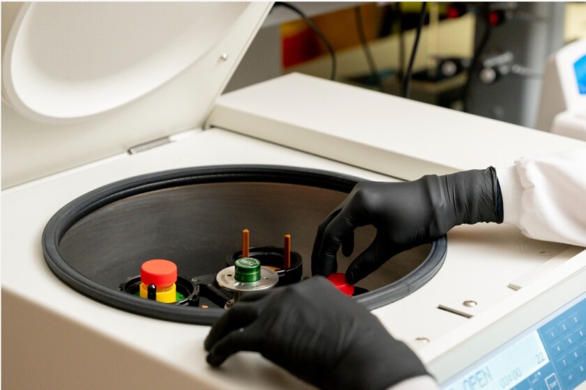 A pair of gloved hands reach into a mysterious piece of science equipment.