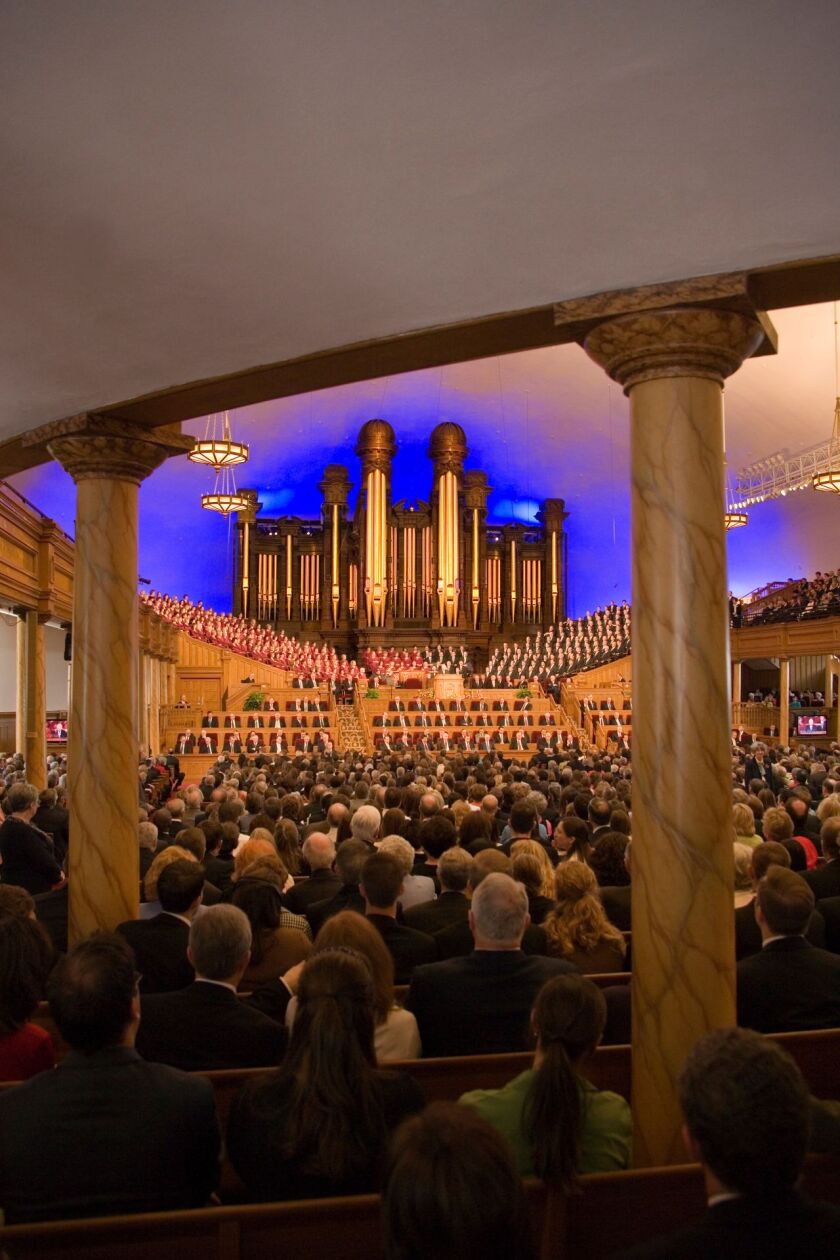 A view from the back of the Salt Lake Tabernacle interior, with people sitting on benches.