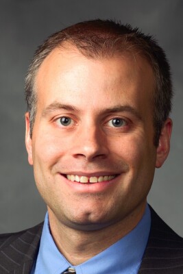Image of white male wearing blue and grey suit with a grey background