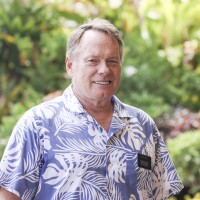 A portrait of Elder Phillip Kimble smiling at the camera with blurred green plants in the background.