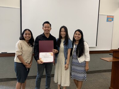 three females and one man smiling at camera and holding up a certificate in a classroom