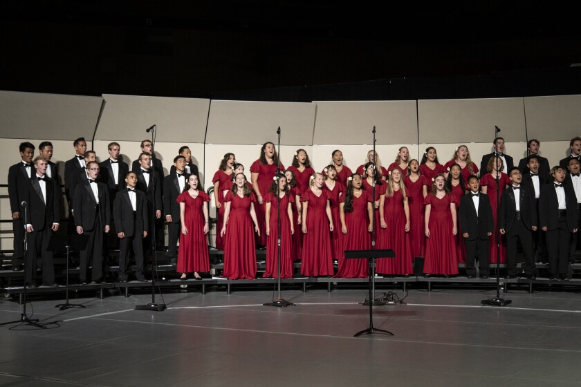 landscape shot of student choir wearing red dresses and black tuxedos standing on onstage risers