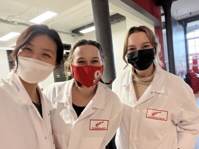Carolyn Chen, Shayden Smith, and Rachel Davis stand side-by-side for a selfie. They're wearing face masks and white lab coats embroidered with the Halloren seal.