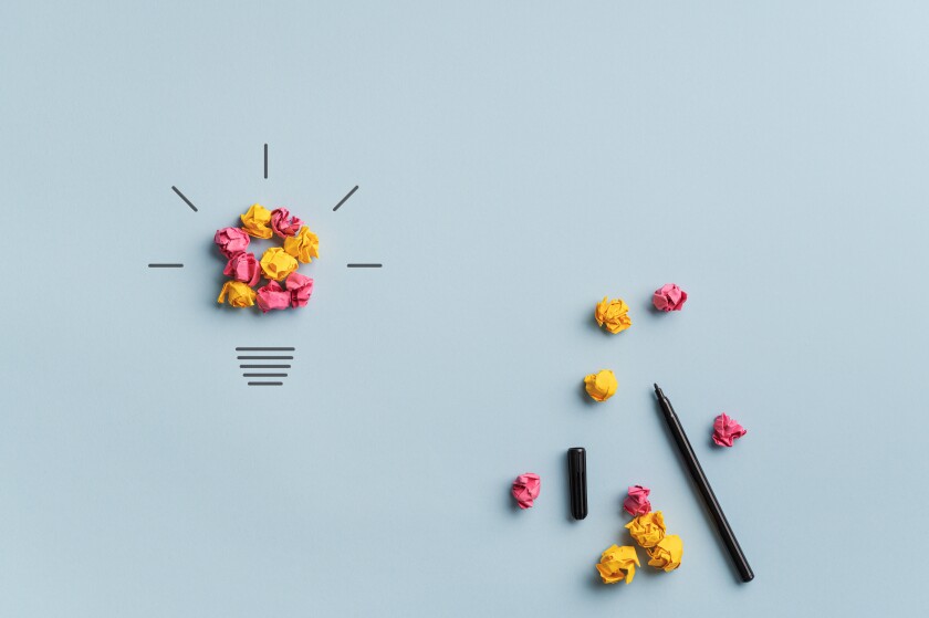 A group of crumpled up papers are arranged into the shape of a light bulb, and little lines are drawn around it to symbolize light. An uncapped marker lays to the side with extra crumpled papers.
