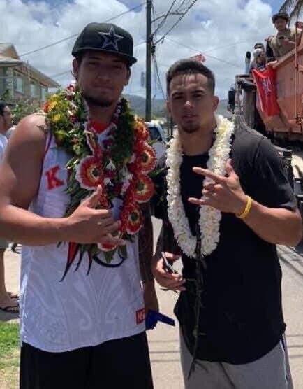 Alohi Gilman and Bradlee Anae stand together in front of a parade of people in Laie.