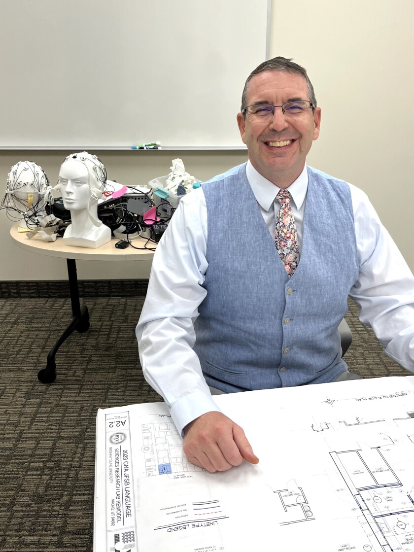 Troy Cox sitting in the Language Sciences Laboratory with floor plans and equipment from the lab.