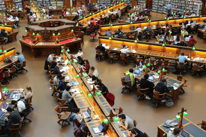 Library full of students studying on computers and reading.