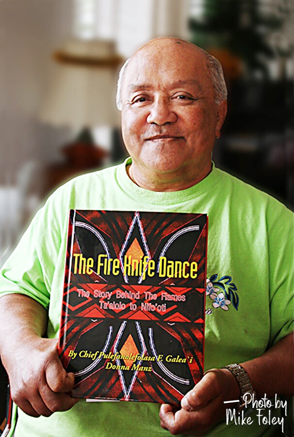 Pulefano Galea'i in a green T-shirt holding his book he wrote about fire knife dancing.