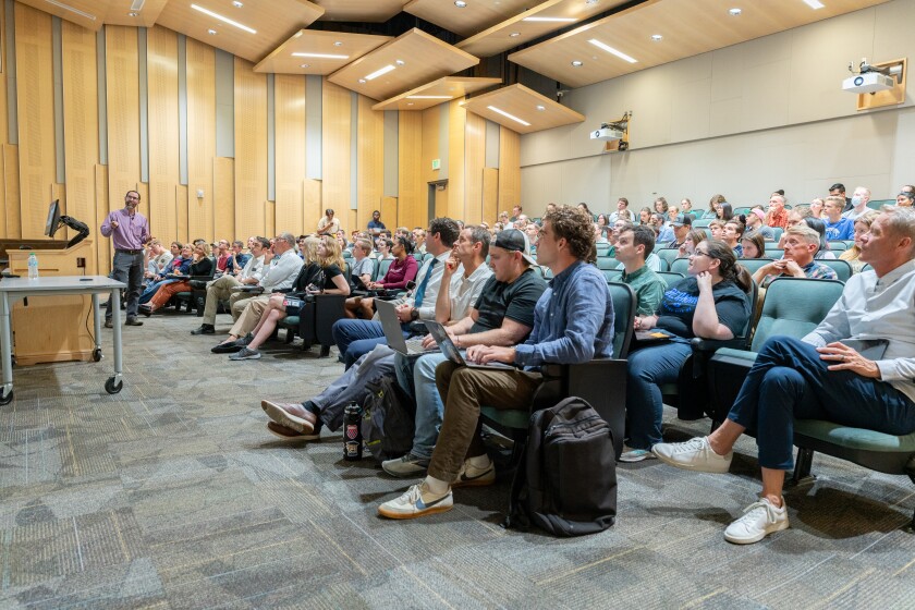 A group of students in a lecture hall sit while watching Dr. Seeley present.