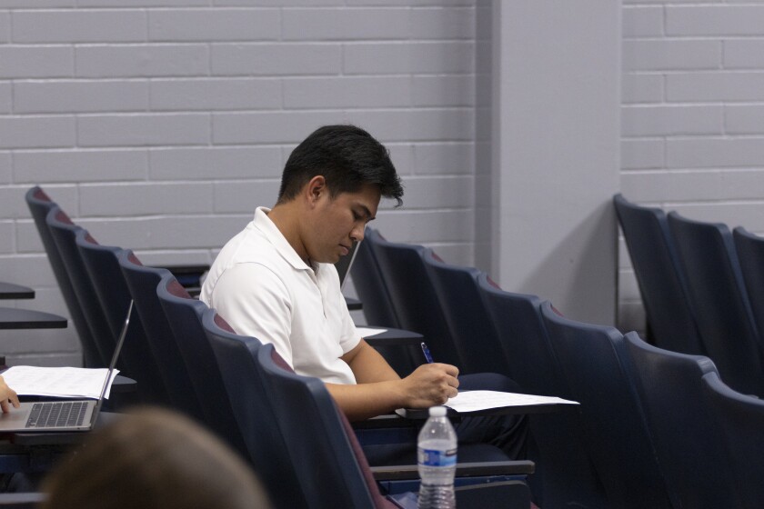 A man sitting in theater seats writes on a paper on the fold out desk