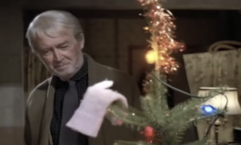 A movie clip from "Mr. Krueger's Christmas" of the actor playing Mr. Krueger standing behind a Christmas tree.