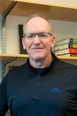 Dr. Johnston, a pale man with glasses wearing a black BYU Public Health zip-up jacket smiles.