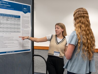 Woman points at her research poster while another woman watches.