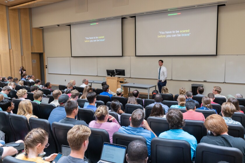 A group of students sit in a lecture hall where Matt Bailey presents at the front.