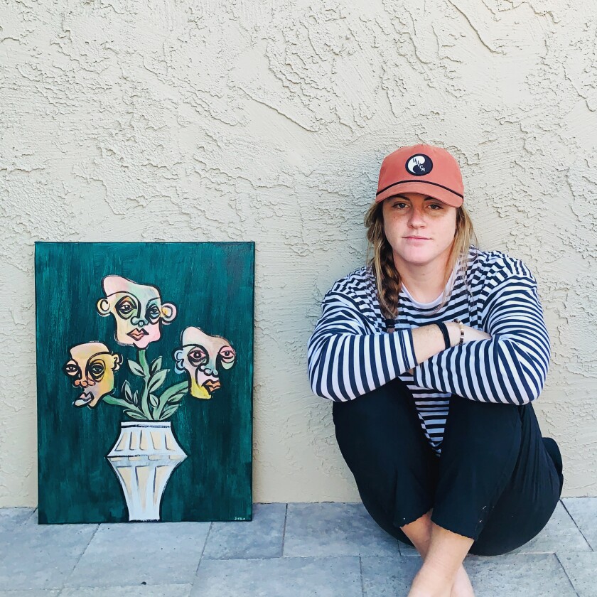 picture of girl wearing a baseball cap and striped shirt sitting next to a canvas painting of a vase with heads instead of flowers coming out of it