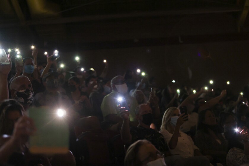 People in a crowd hold up their phones with flashlights on them.