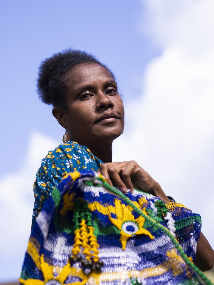 A woman stand outside wrapped in a multicolored fabric.