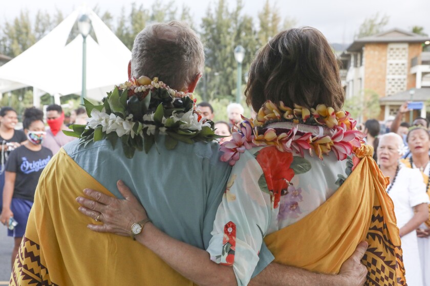 John and Susan Tanner stand with arms around each other with leis and a traditional Hawaiian yellow wrap.