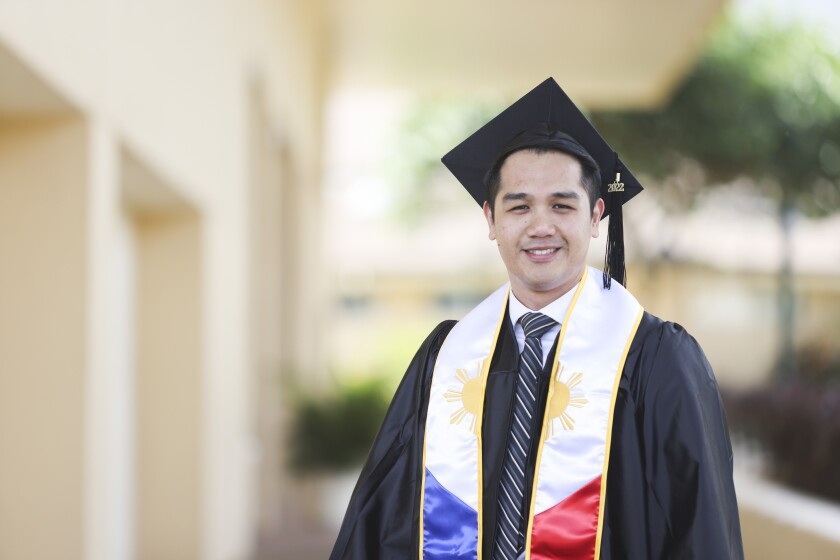 Micah wears graduation cap and gown as he stands outdoors.