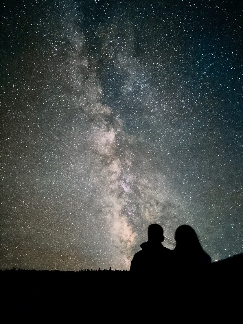 Two silhouetted people sit and look at the Milky Way Galaxy in the night sky