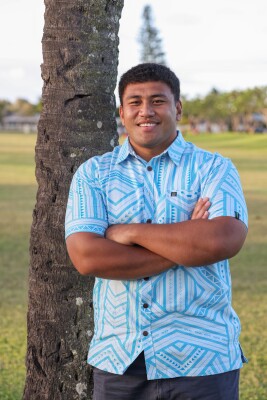 Kelvin Uili with arms crossed, leaning on a coconut tree