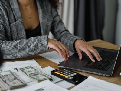 Woman typing on a computer with money and a calculator by her