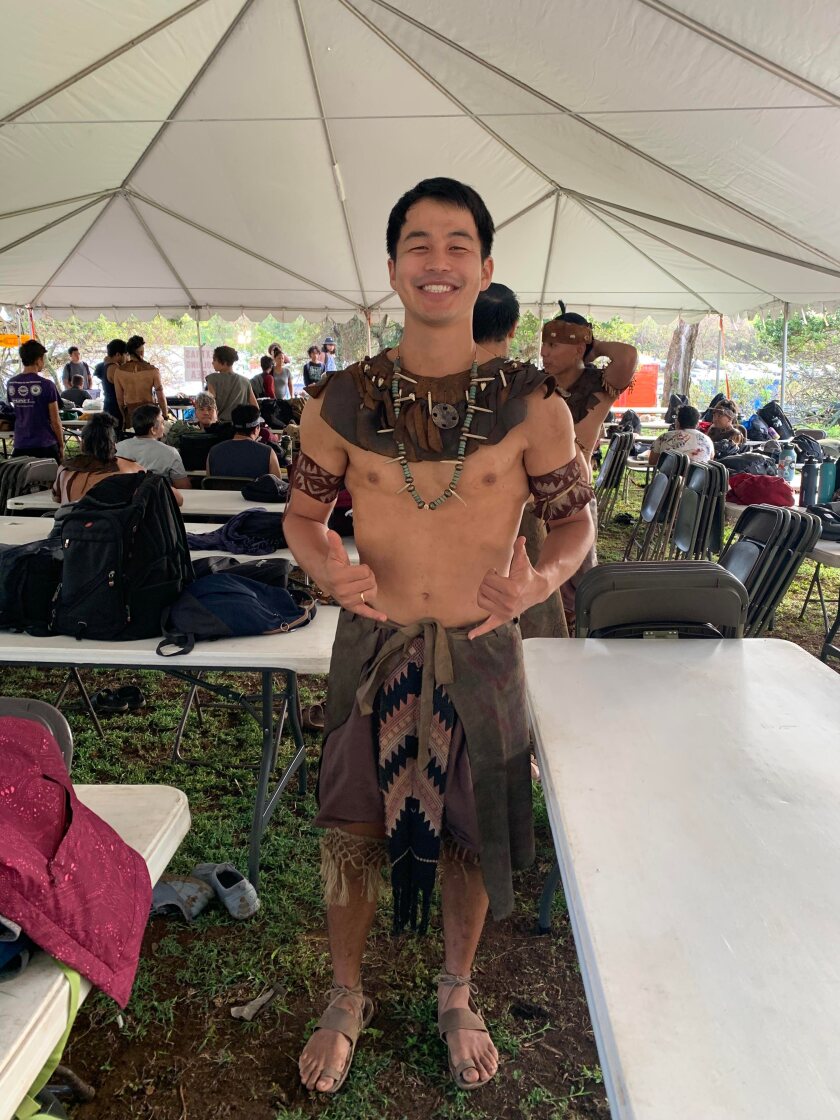 An actor in the Book of Mormon videos stands in costume looking like a native warrior under a tent.