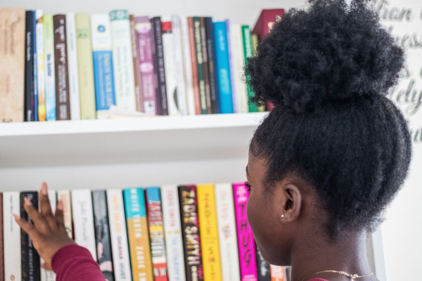 Black girl picking book off of a book shelf full of books