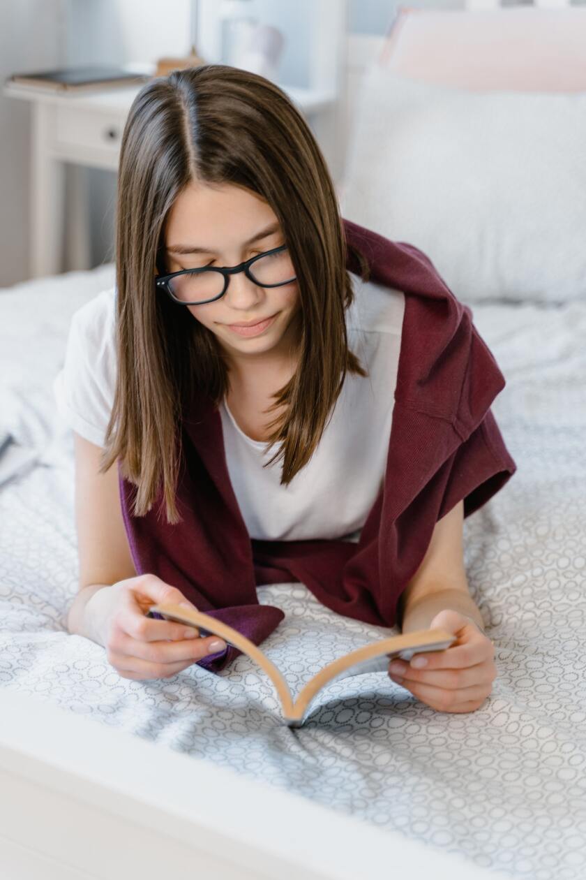 Teenager reading a book on her bed.