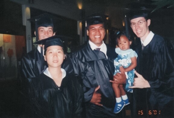 Four graduates smile while one graduate holds a baby.