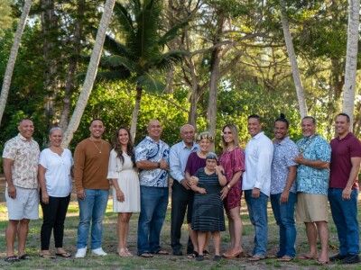 A family of 11 grown children stand in a line outside on the grass with their parents in middle.