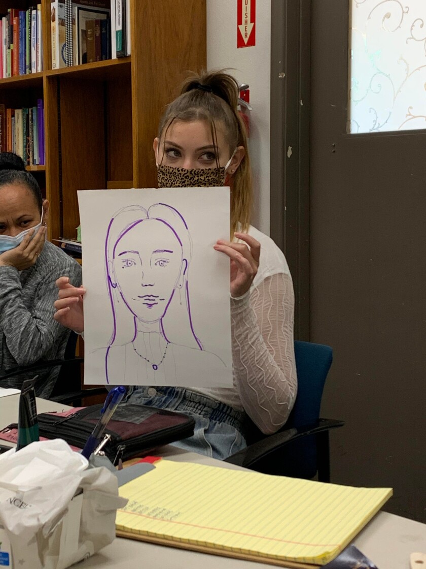 A girl wearing a white long-sleeve shirt and jeans with a cheetah print mask and a ponytail holding up a portrait of her face made on white paper with purple paint.