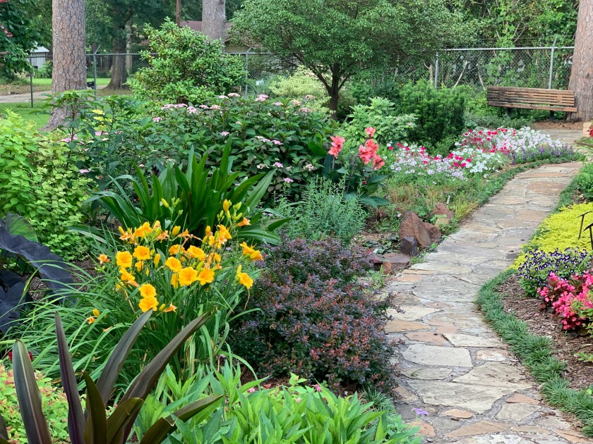 A narrow stone path that is lined with all sorts of flowers, bushes, and trees.