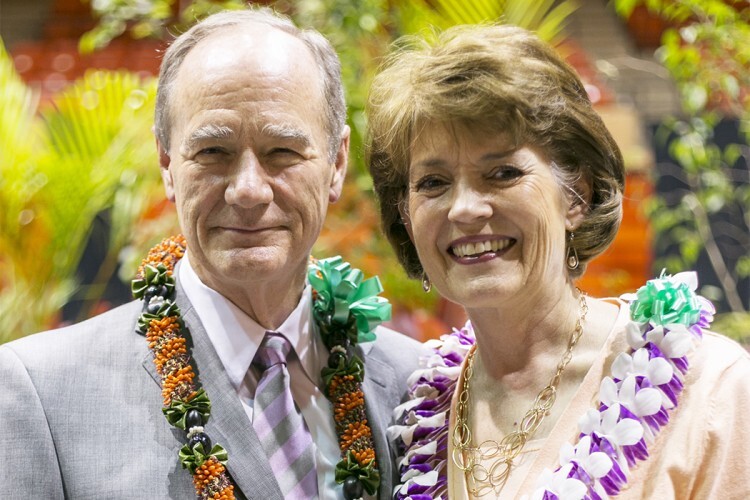 John Tanner wearing a green and orange lei standing next to Susan Tanner wearing a purple and white lei