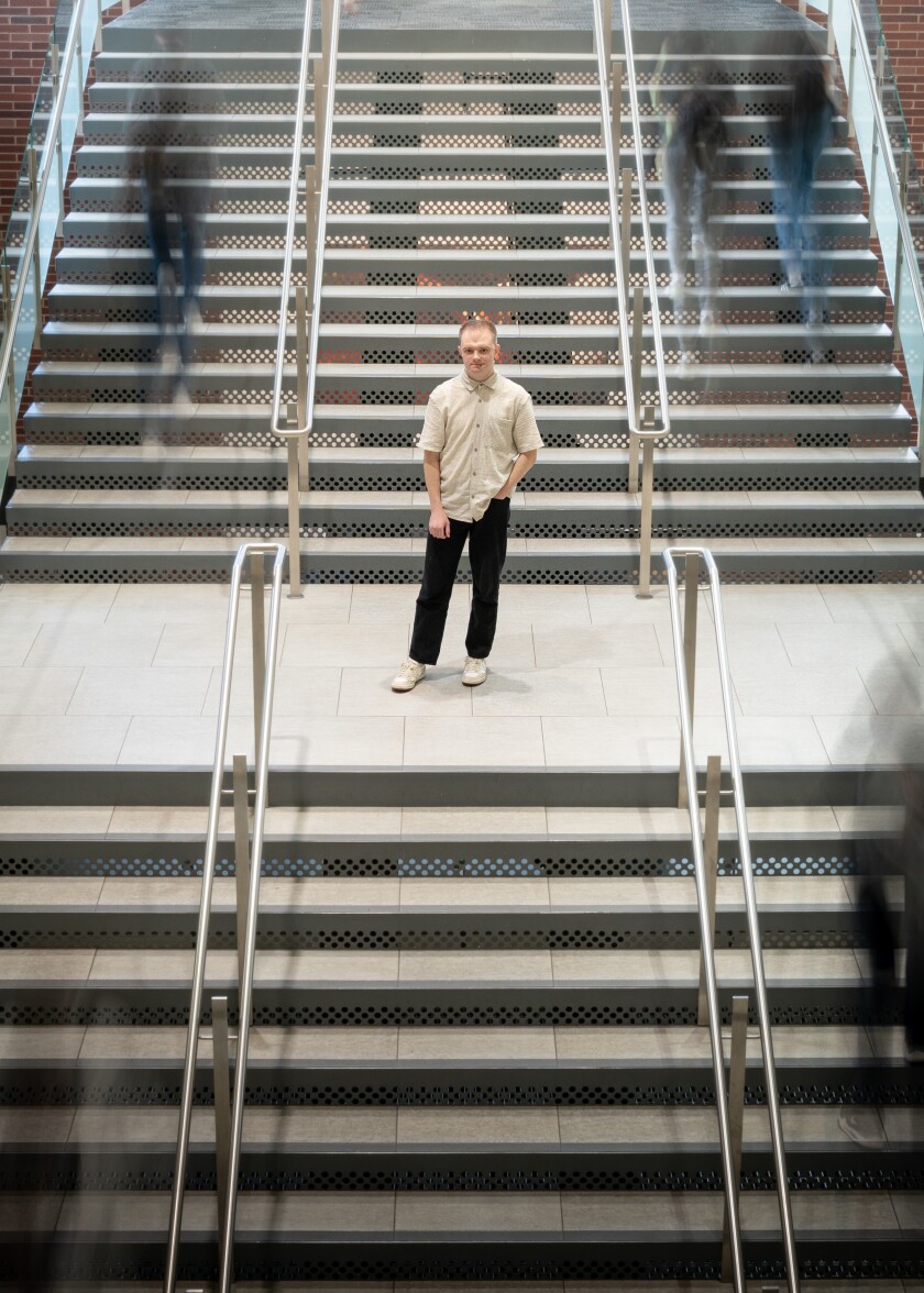 A man stands on a staircase. People walk past him.