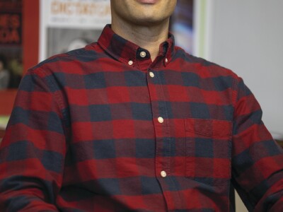 Mason Allred sitting on a black chair wearing a blue and red plaid button-up shirt.