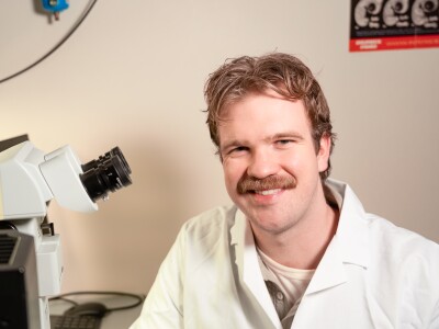 Joshua Wright smiling next to a microscope in a lab.