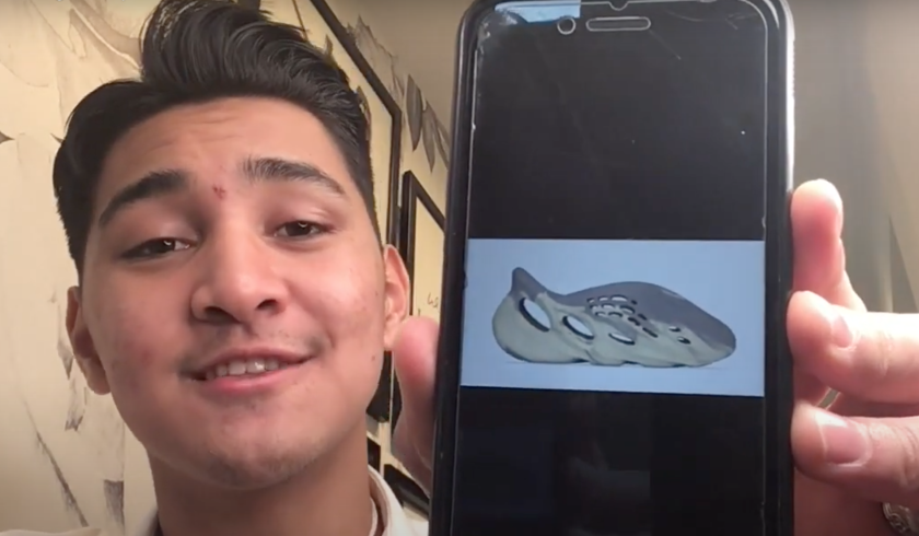 Nathaniel Aiu showing his phone to the screen of a shoe with an off-white background behind him.