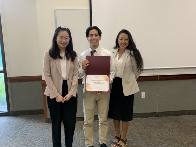 a man standing between two women in suits holding a certificate and smiling at camera