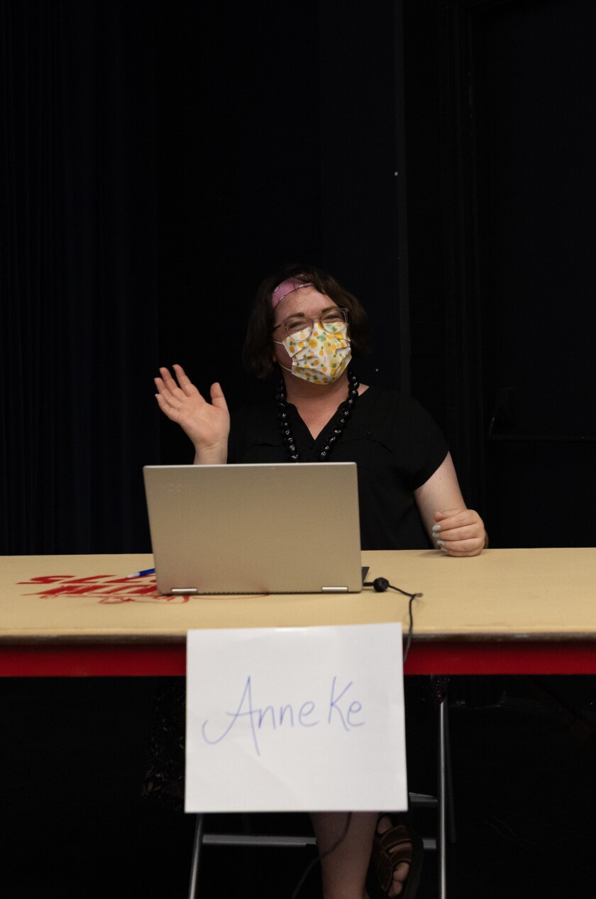 Anneke Garcia, wearing a black shirt, yellow and white floral mask, and pink headband waving at the crowd.