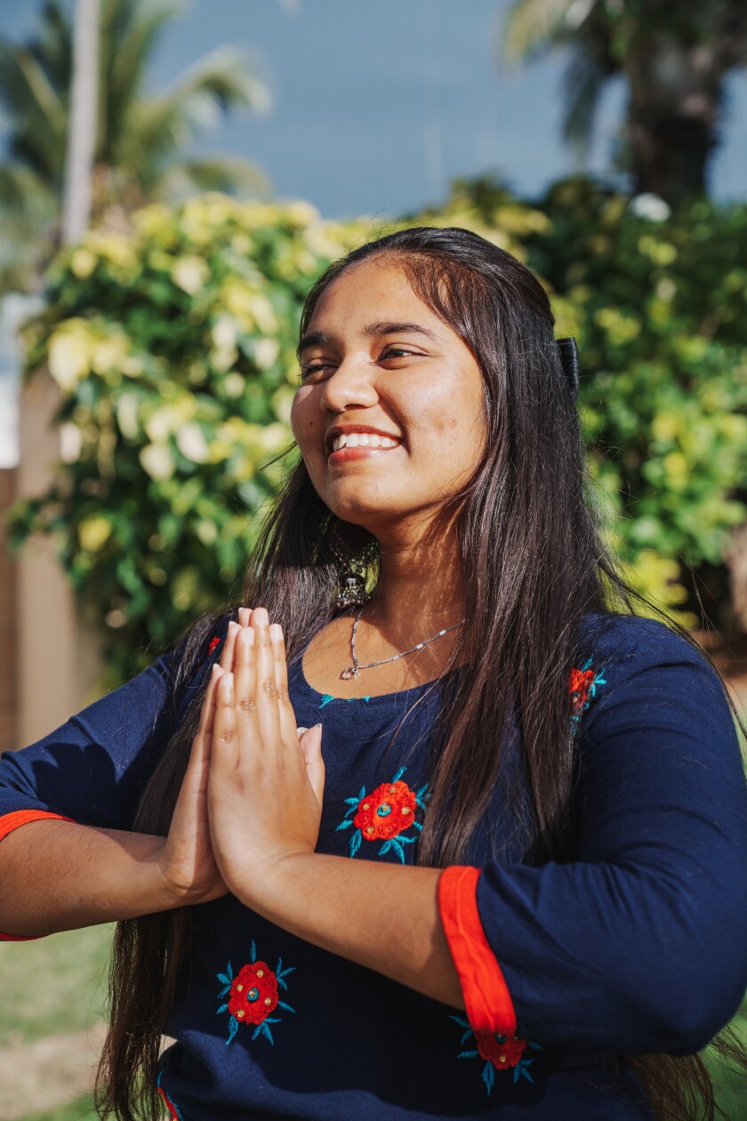 A woman stands outside with her hands in a praying position.